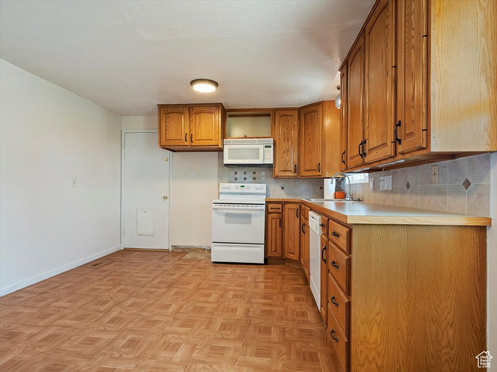 Kitchen with backsplash, white appliances, light parquet flooring, and sink