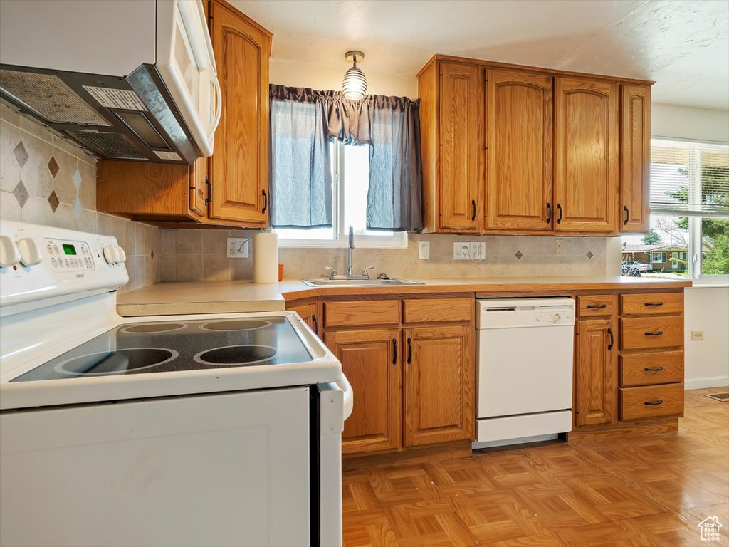 Kitchen featuring wall chimney exhaust hood, sink, white appliances, backsplash, and light parquet floors