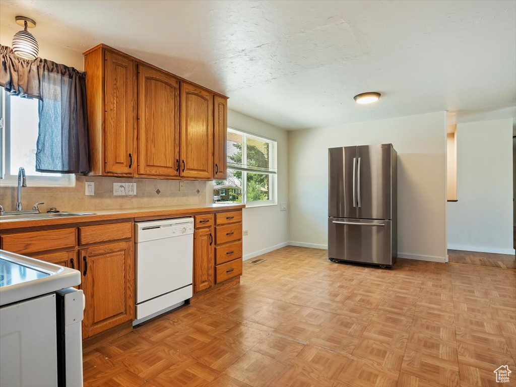 Kitchen featuring stainless steel refrigerator, white dishwasher, sink, and light parquet flooring