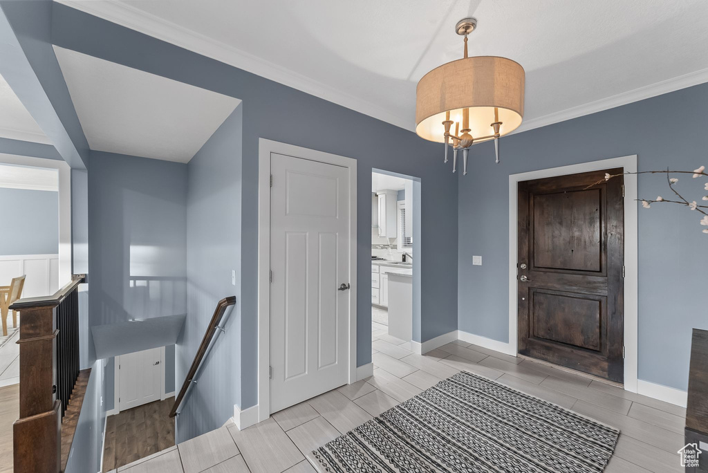 Foyer with crown molding, an inviting chandelier, and light tile floors