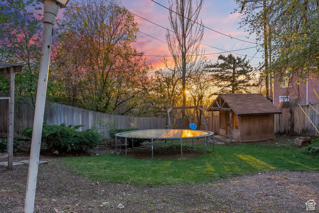 Yard at dusk featuring a trampoline and an outdoor structure