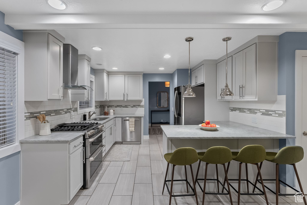 Kitchen featuring tasteful backsplash, pendant lighting, wall chimney range hood, and stainless steel appliances