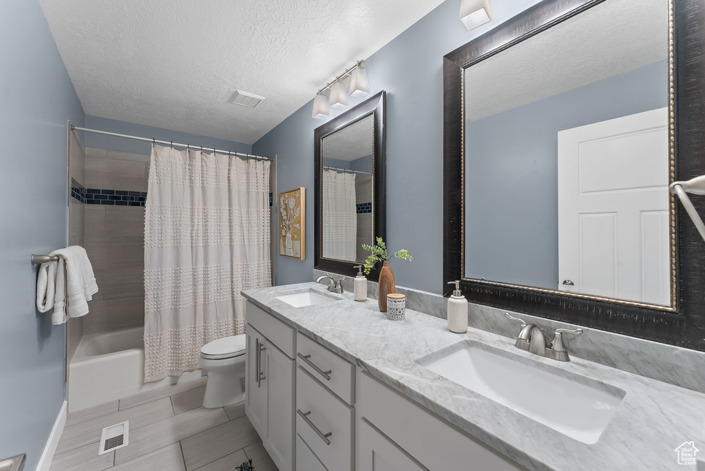 Full bathroom with shower / bath combination with curtain, toilet, double vanity, a textured ceiling, and tile floors
