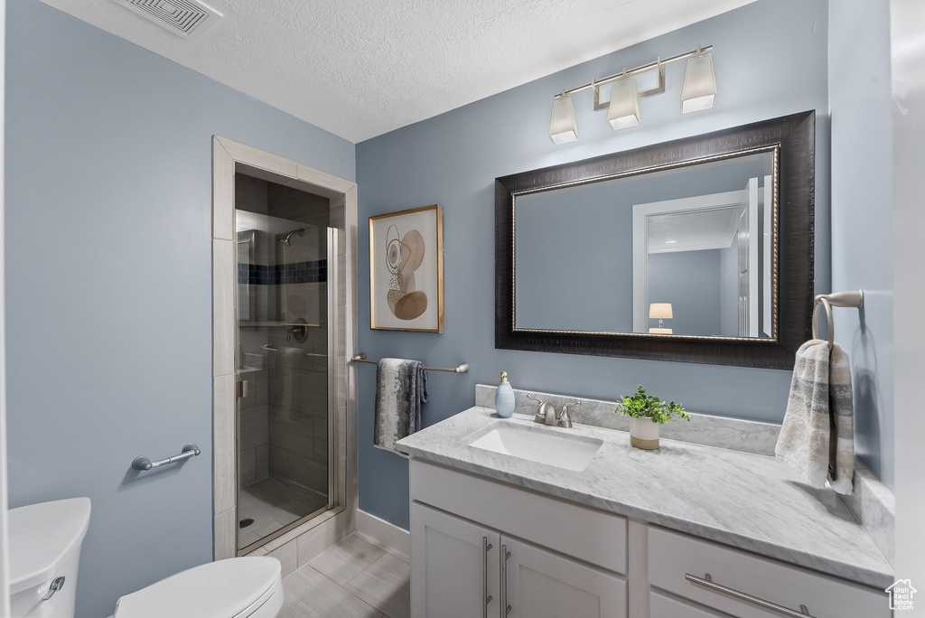 Bathroom with toilet, a textured ceiling, an enclosed shower, vanity, and tile floors
