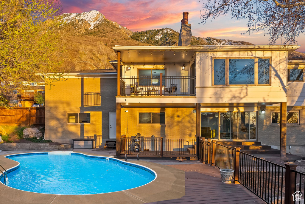 Back house at dusk with a mountain view, a balcony, a patio area, and a fenced in pool