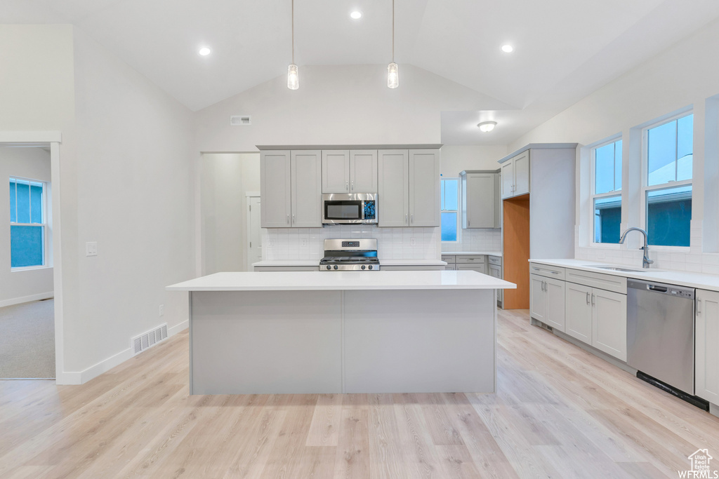 Kitchen featuring appliances with stainless steel finishes, light hardwood / wood-style flooring, a kitchen island, and backsplash