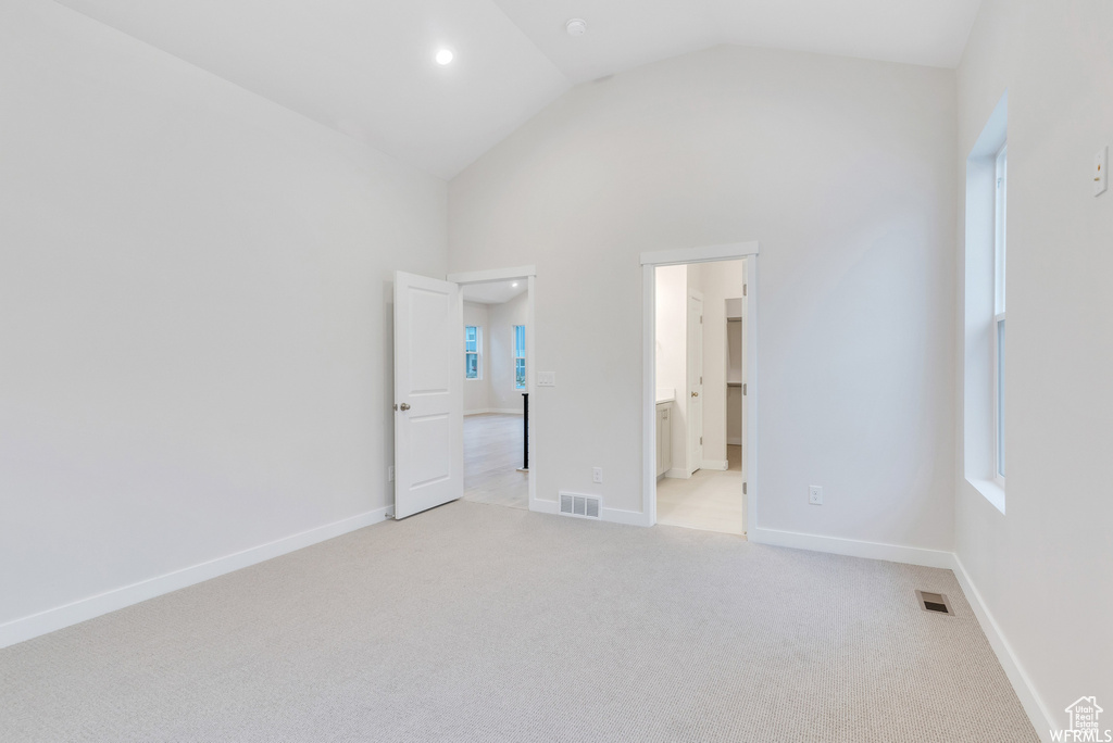 Unfurnished bedroom with light colored carpet, ensuite bath, and high vaulted ceiling