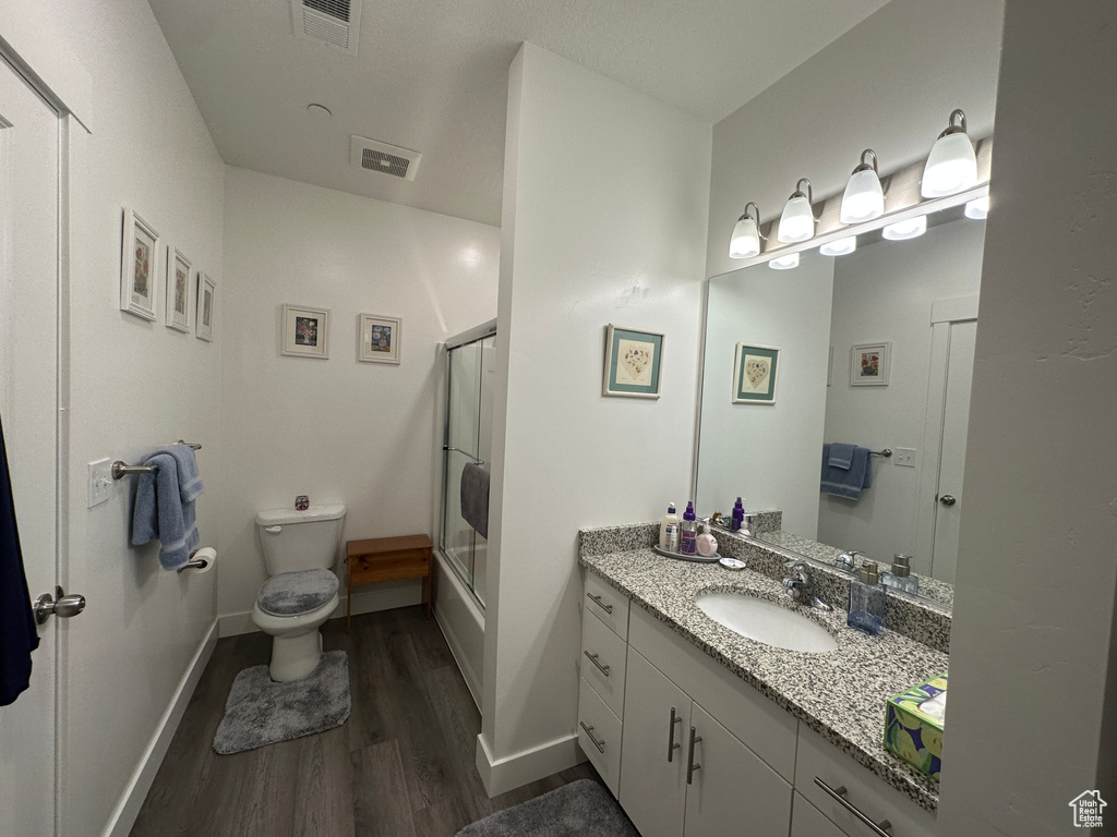 Full bathroom with hardwood / wood-style floors, vanity, toilet, and combined bath / shower with glass door