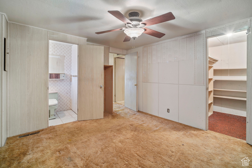Unfurnished bedroom with light colored carpet, a walk in closet, ceiling fan, and ensuite bathroom