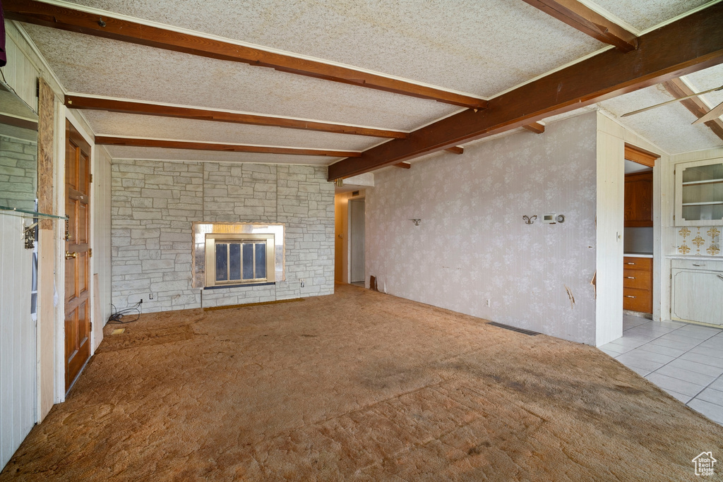Unfurnished living room featuring a stone fireplace, light colored carpet, vaulted ceiling with beams, and a textured ceiling