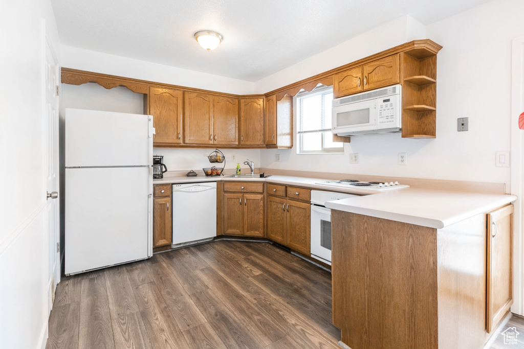 Kitchen featuring white appliances, dark hardwood / wood-style flooring, kitchen peninsula, and sink