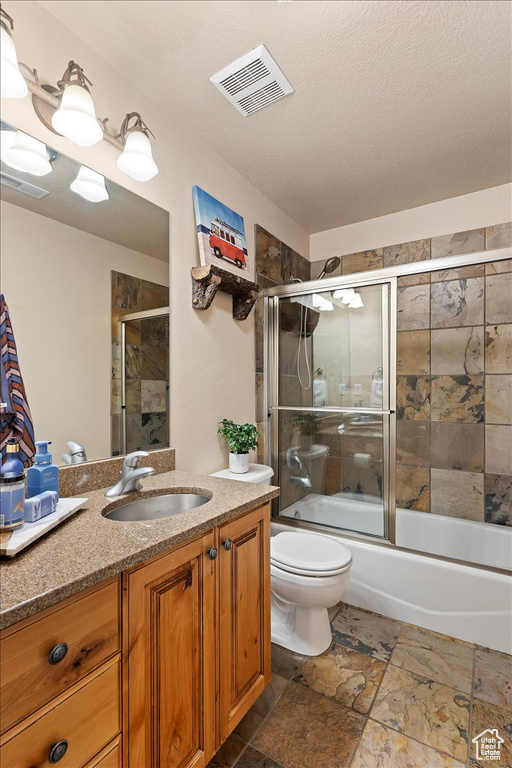 Full bathroom featuring vanity, enclosed tub / shower combo, tile flooring, toilet, and a textured ceiling