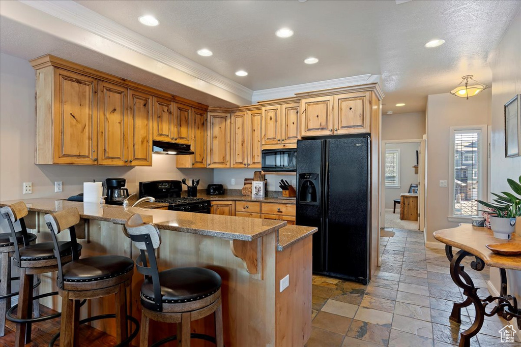 Kitchen featuring light stone countertops, kitchen peninsula, black appliances, a breakfast bar, and light tile floors