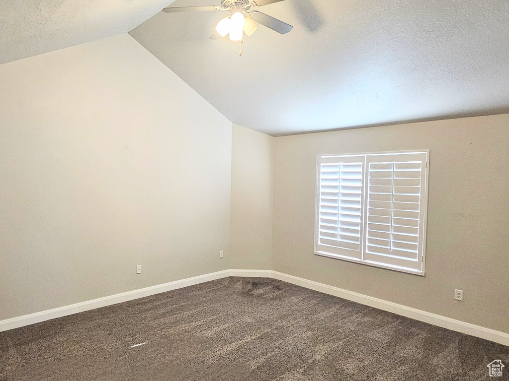 Spare room featuring ceiling fan, dark carpet, a textured ceiling, and lofted ceiling