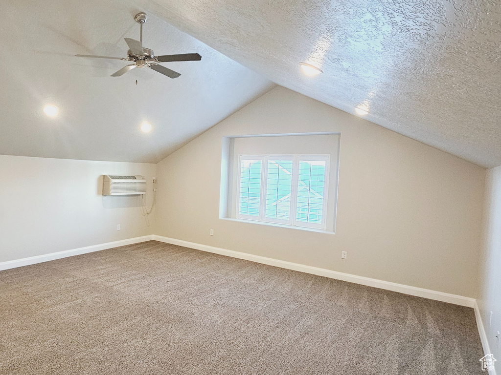 Additional living space featuring ceiling fan, carpet, a textured ceiling, a wall mounted AC, and lofted ceiling