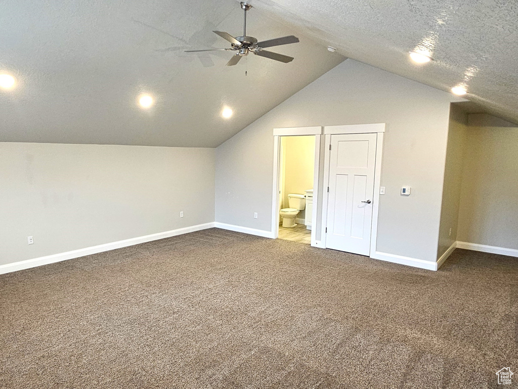 Bonus room featuring a textured ceiling, vaulted ceiling, and dark colored carpet