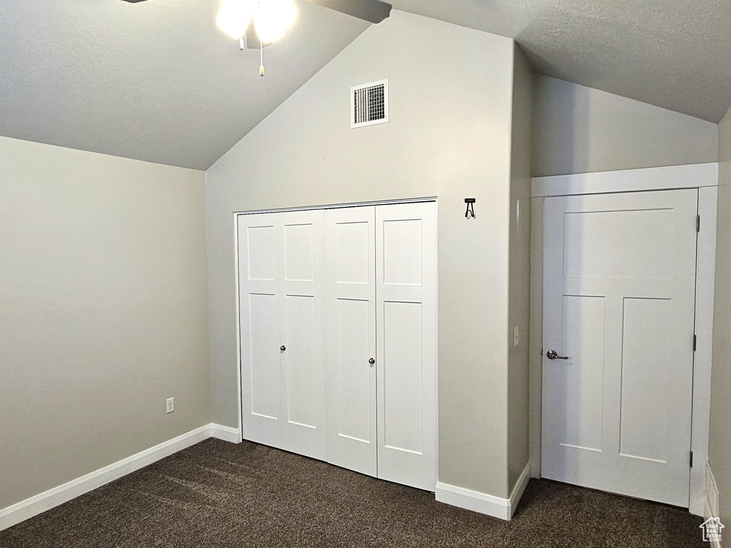 Unfurnished bedroom featuring a closet, dark carpet, ceiling fan, and lofted ceiling