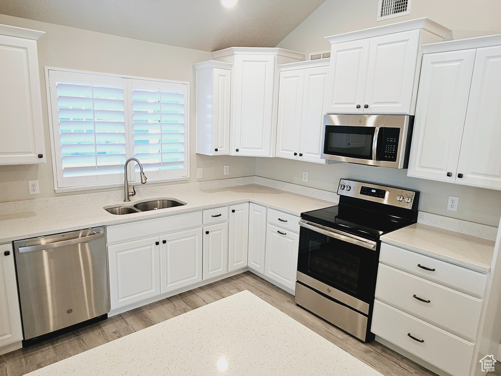 Kitchen with white cabinets, light hardwood / wood-style flooring, stainless steel appliances, vaulted ceiling, and sink