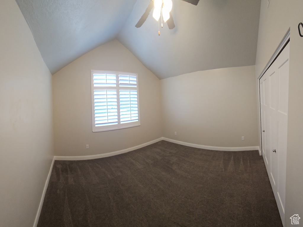 Interior space featuring ceiling fan, vaulted ceiling, and dark carpet