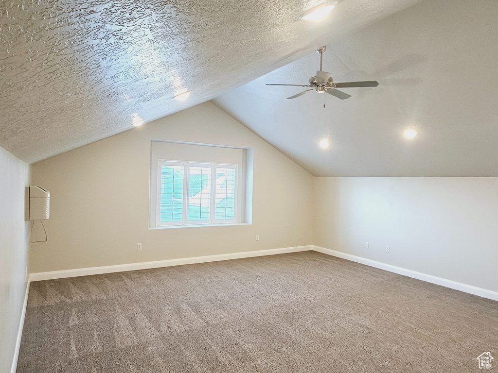 Bonus room with vaulted ceiling, dark colored carpet, ceiling fan, and a textured ceiling