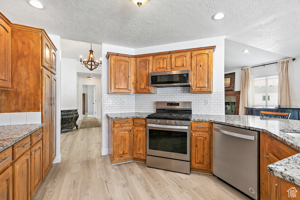 Kitchen with tasteful backsplash, stainless steel appliances, light stone countertops, light hardwood / wood-style flooring, and an inviting chandelier