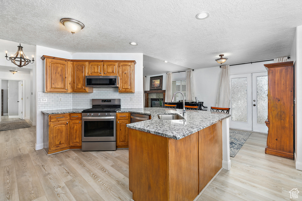 Kitchen with light stone countertops, light hardwood / wood-style flooring, stainless steel appliances, tasteful backsplash, and sink