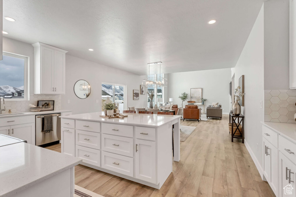 Kitchen with light wood-type flooring, dishwasher, tasteful backsplash, and white cabinetry