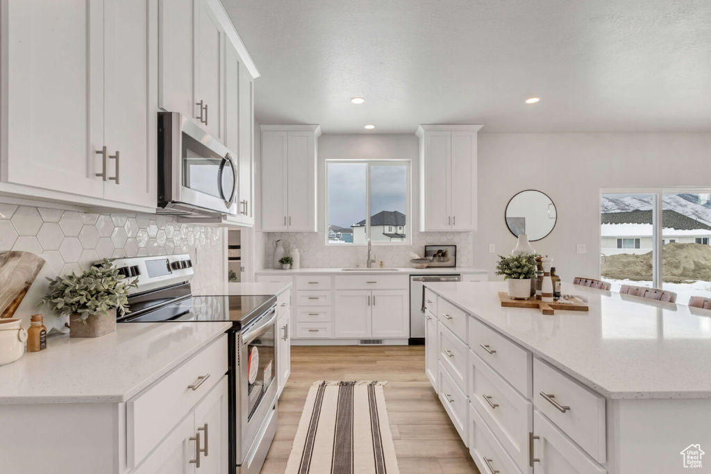 Kitchen featuring white cabinets, a healthy amount of sunlight, backsplash, and stainless steel appliances