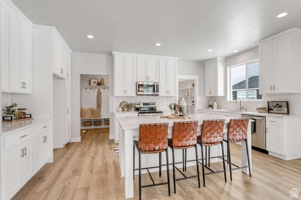 Kitchen featuring a kitchen island, light hardwood / wood-style flooring, stainless steel appliances, tasteful backsplash, and white cabinets