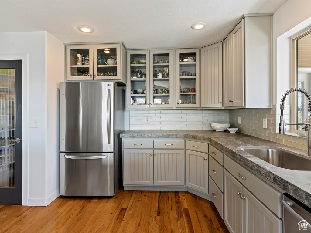 Kitchen with appliances with stainless steel finishes, sink, backsplash, light wood-type flooring, and gray cabinetry