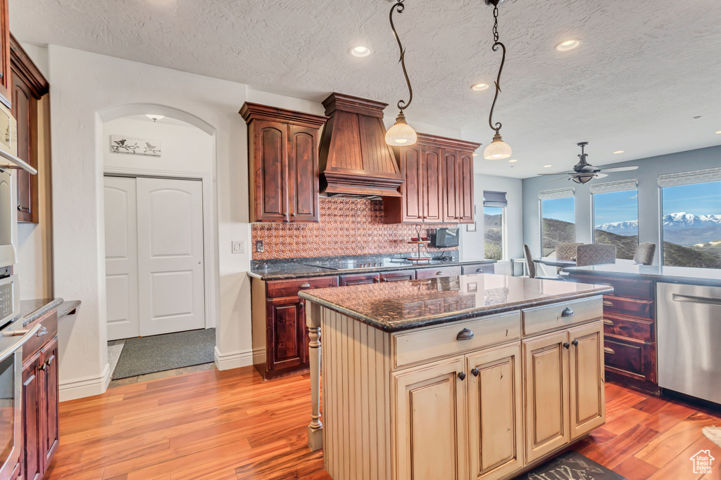Kitchen featuring a center island, backsplash, custom range hood, stainless steel appliances, and ceiling fan