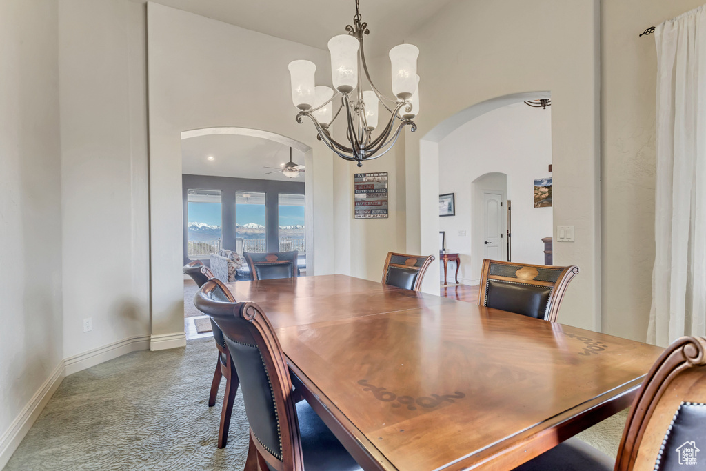 Dining area featuring ceiling fan with notable chandelier, high vaulted ceiling, and carpet flooring