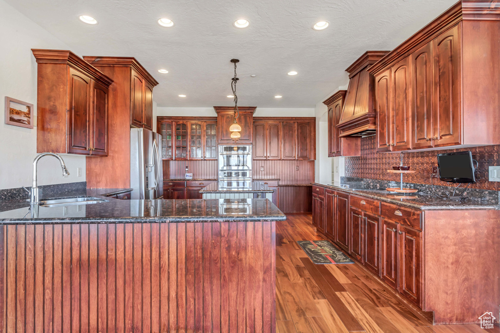 Kitchen with pendant lighting, hardwood / wood-style floors, stainless steel appliances, sink, and dark stone counters