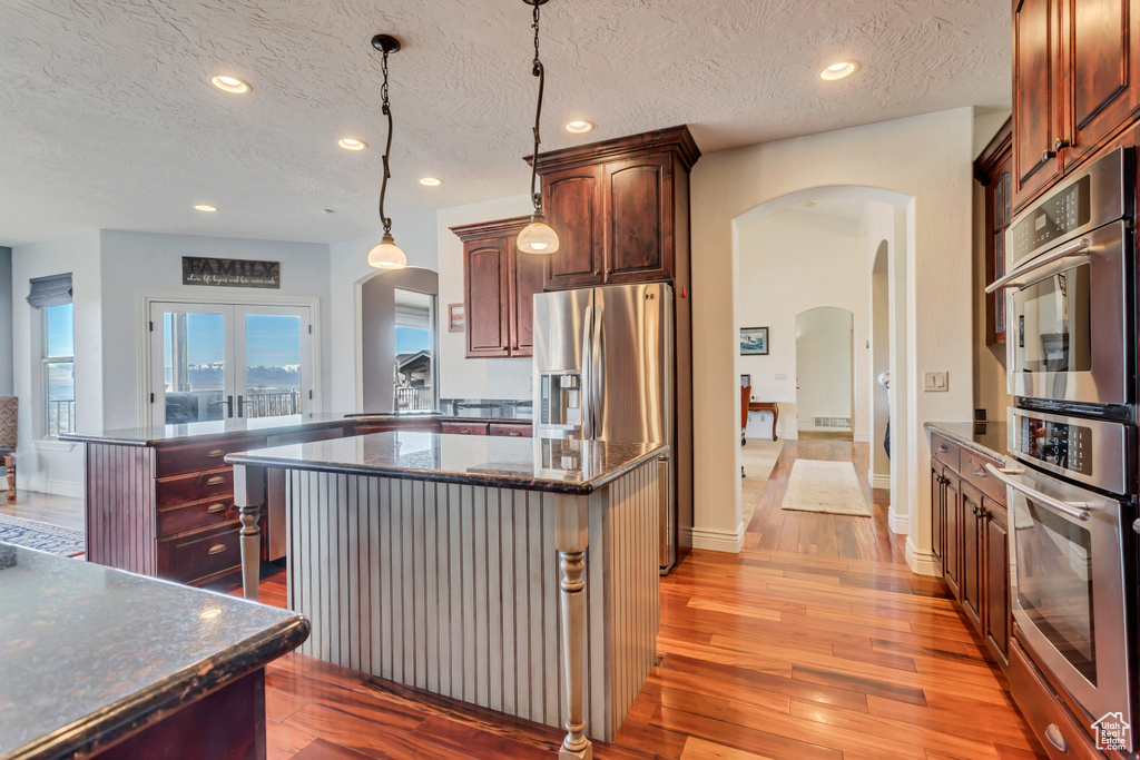 Kitchen featuring a center island, pendant lighting, light hardwood / wood-style flooring, stainless steel appliances, and dark stone countertops
