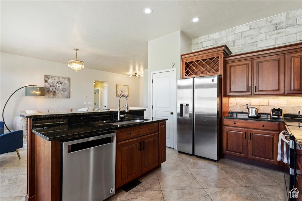 Kitchen featuring hanging light fixtures, stainless steel appliances, light tile floors, sink, and an island with sink