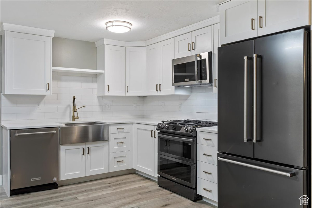 Kitchen with backsplash, appliances with stainless steel finishes, light hardwood / wood-style floors, and sink