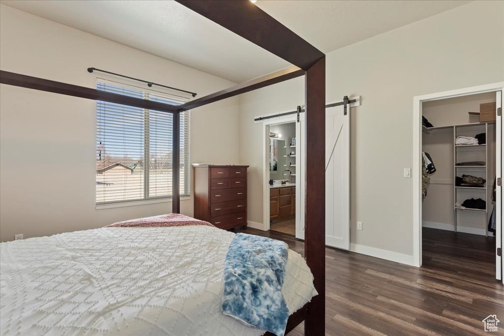 Bedroom featuring a closet, a barn door, ensuite bath, dark wood-type flooring, and a spacious closet