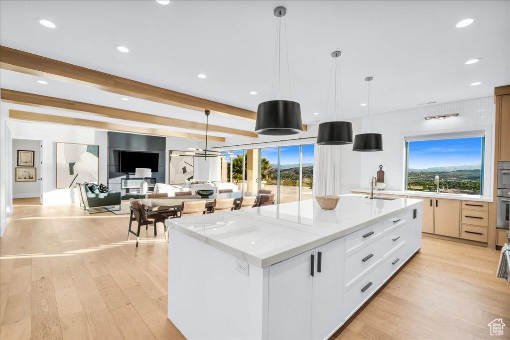 Kitchen featuring pendant lighting, a kitchen island with sink, white cabinets, light stone counters, and light hardwood / wood-style floors