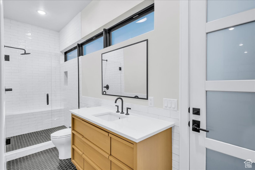 Bathroom with walk in shower, vanity, tile walls, tile flooring, and toilet