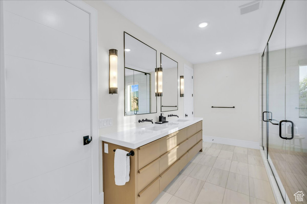 Bathroom featuring a shower with door, large vanity, dual sinks, and tile flooring