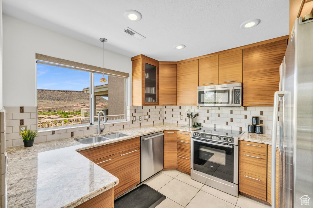 Kitchen featuring sink, backsplash, light tile flooring, stainless steel appliances, and light stone countertops