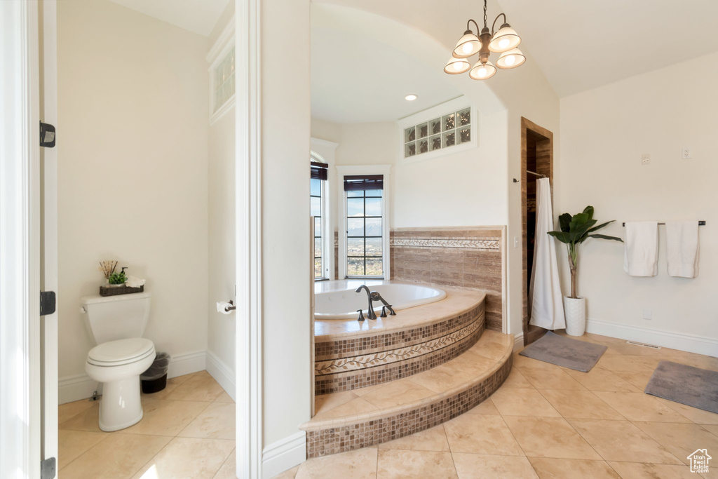 Bathroom featuring a notable chandelier, tile floors, toilet, and tiled tub