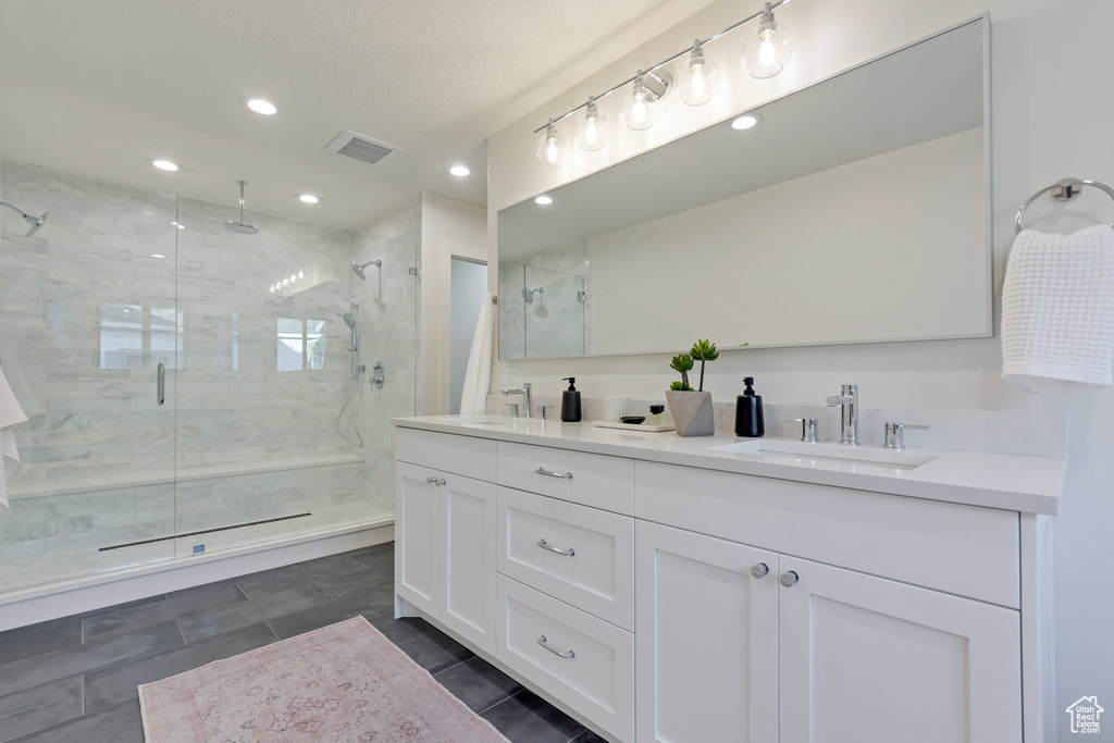 Bathroom featuring a shower with door, tile flooring, dual vanity, and a textured ceiling