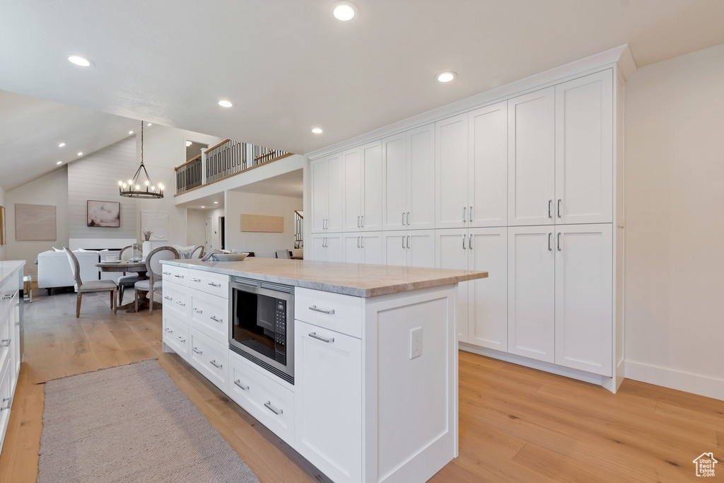 Kitchen featuring light wood-type flooring, vaulted ceiling, stainless steel microwave, and white cabinetry