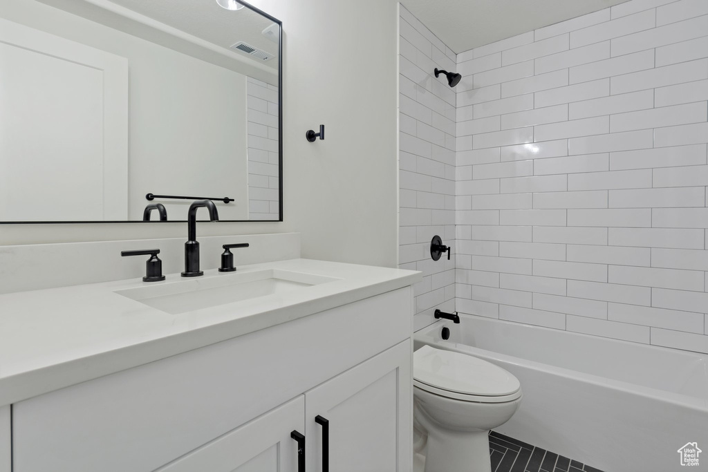Full bathroom with tile floors, oversized vanity, tiled shower / bath combo, and toilet