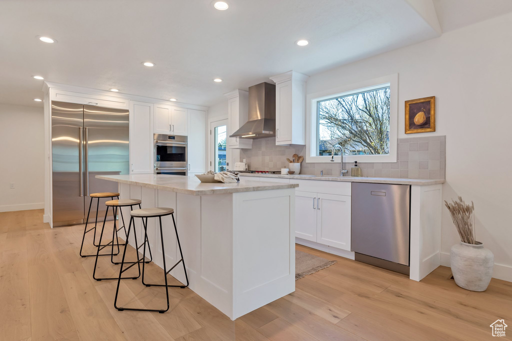 Kitchen featuring white cabinets, wall chimney range hood, tasteful backsplash, and stainless steel appliances