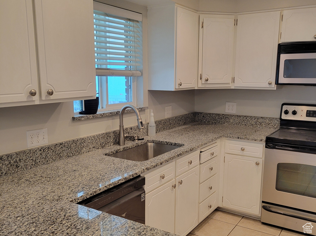 Kitchen featuring light stone countertops, light tile flooring, stainless steel electric range, white cabinets, and sink