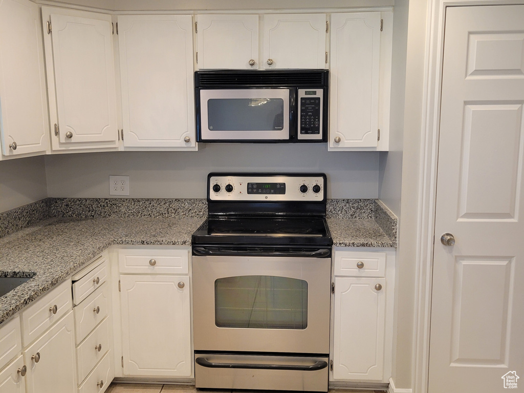 Kitchen with appliances with stainless steel finishes, white cabinetry, and light tile flooring