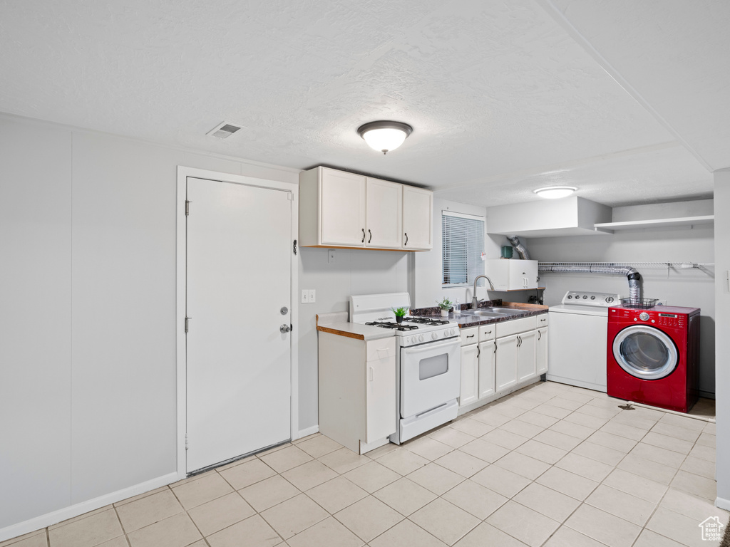 Kitchen featuring light tile flooring, white gas range oven, independent washer and dryer, white cabinetry, and sink