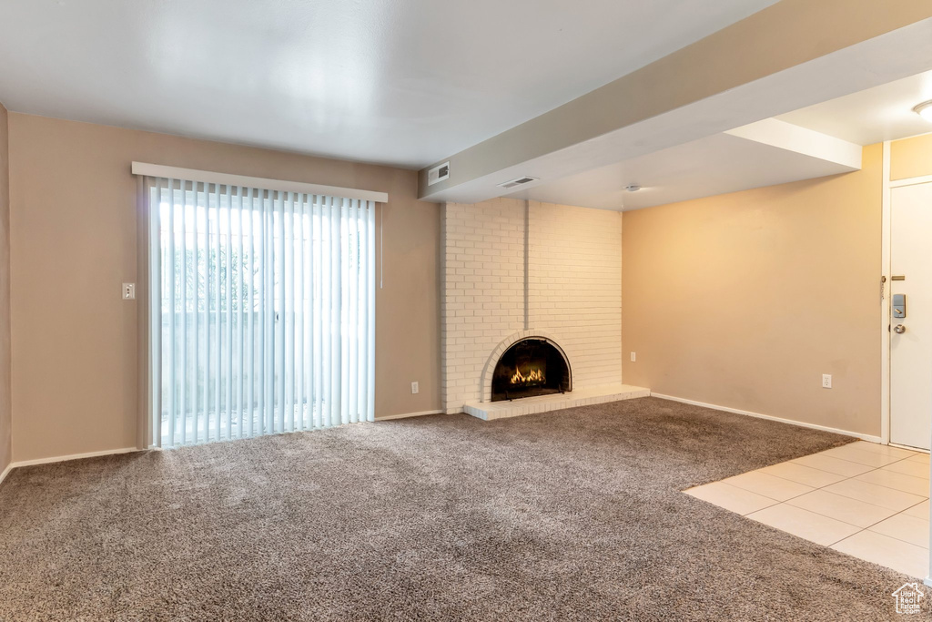 Unfurnished living room featuring a fireplace, brick wall, and carpet flooring
